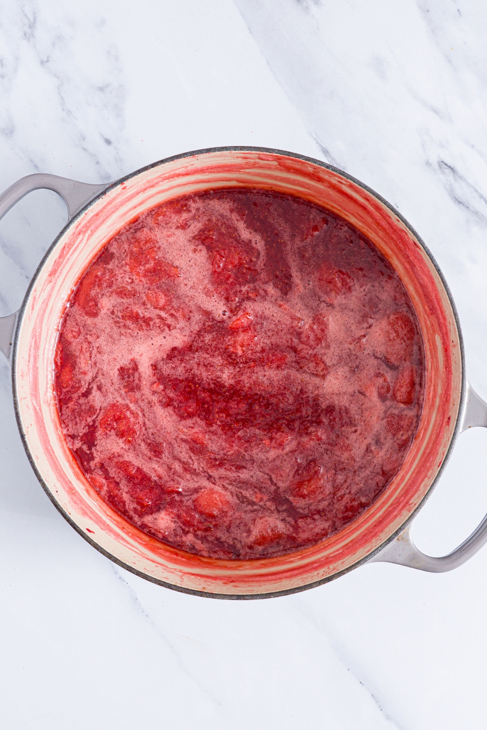 A dutch oven with boiling strawberry jam. The pot is on a marble counter.