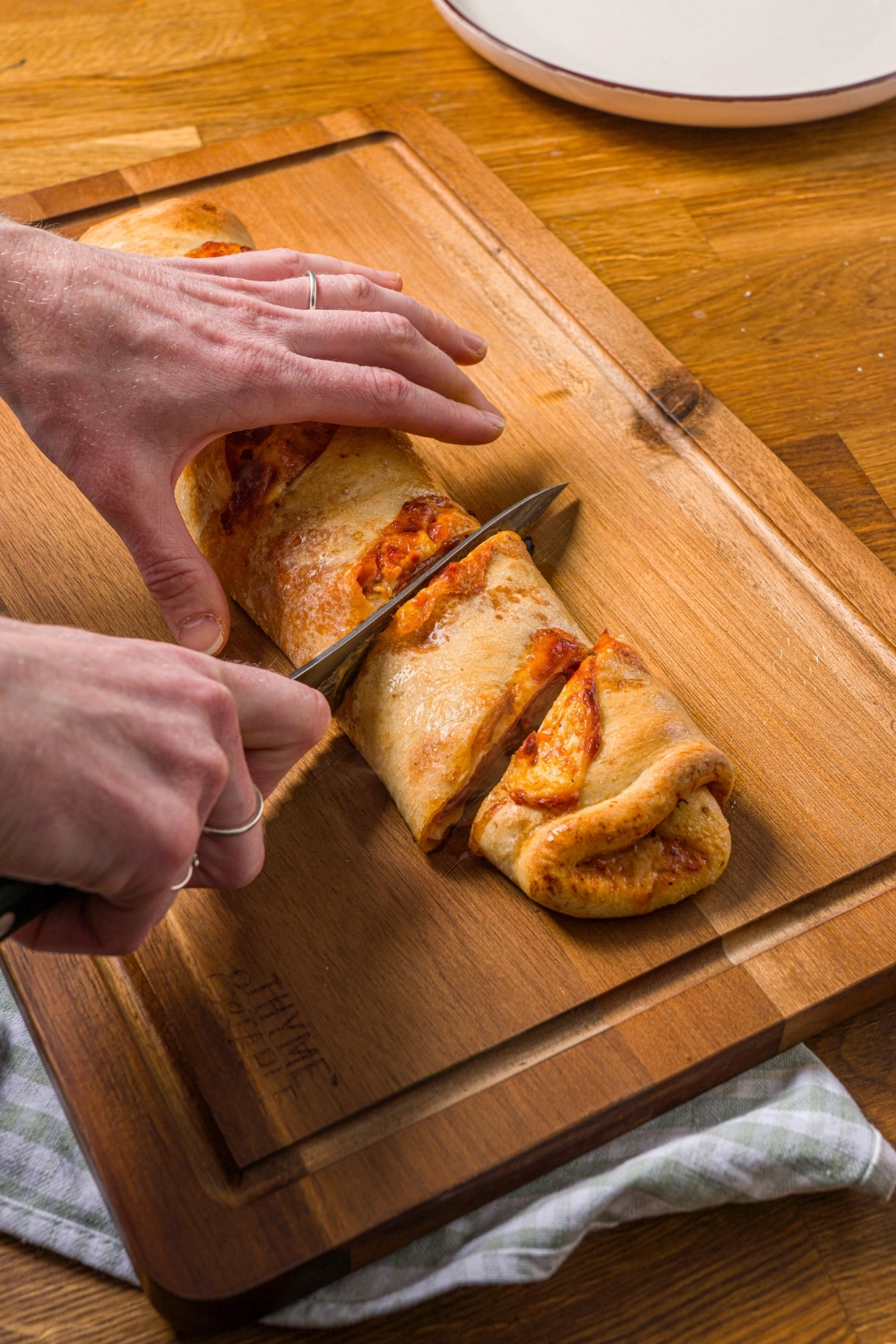 A wooden cutting board with a whole baked stromboli being cut into slices. The board is on a wood counter.