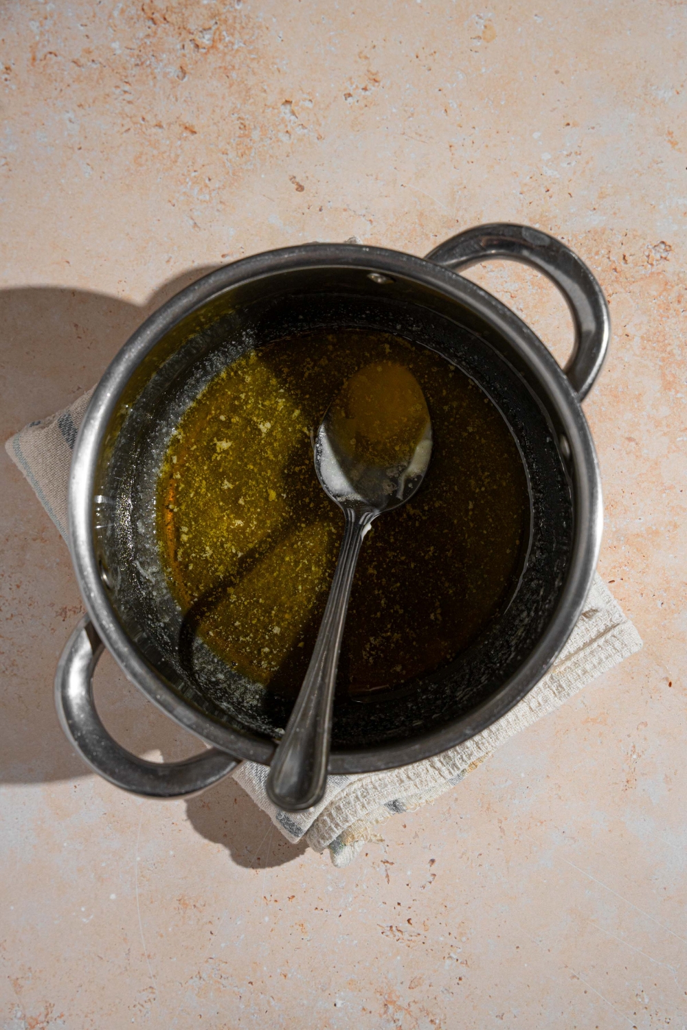 A saucepan with cooked butter glaze with a spoon in the saucepan. The saucepan is on a tan counter.