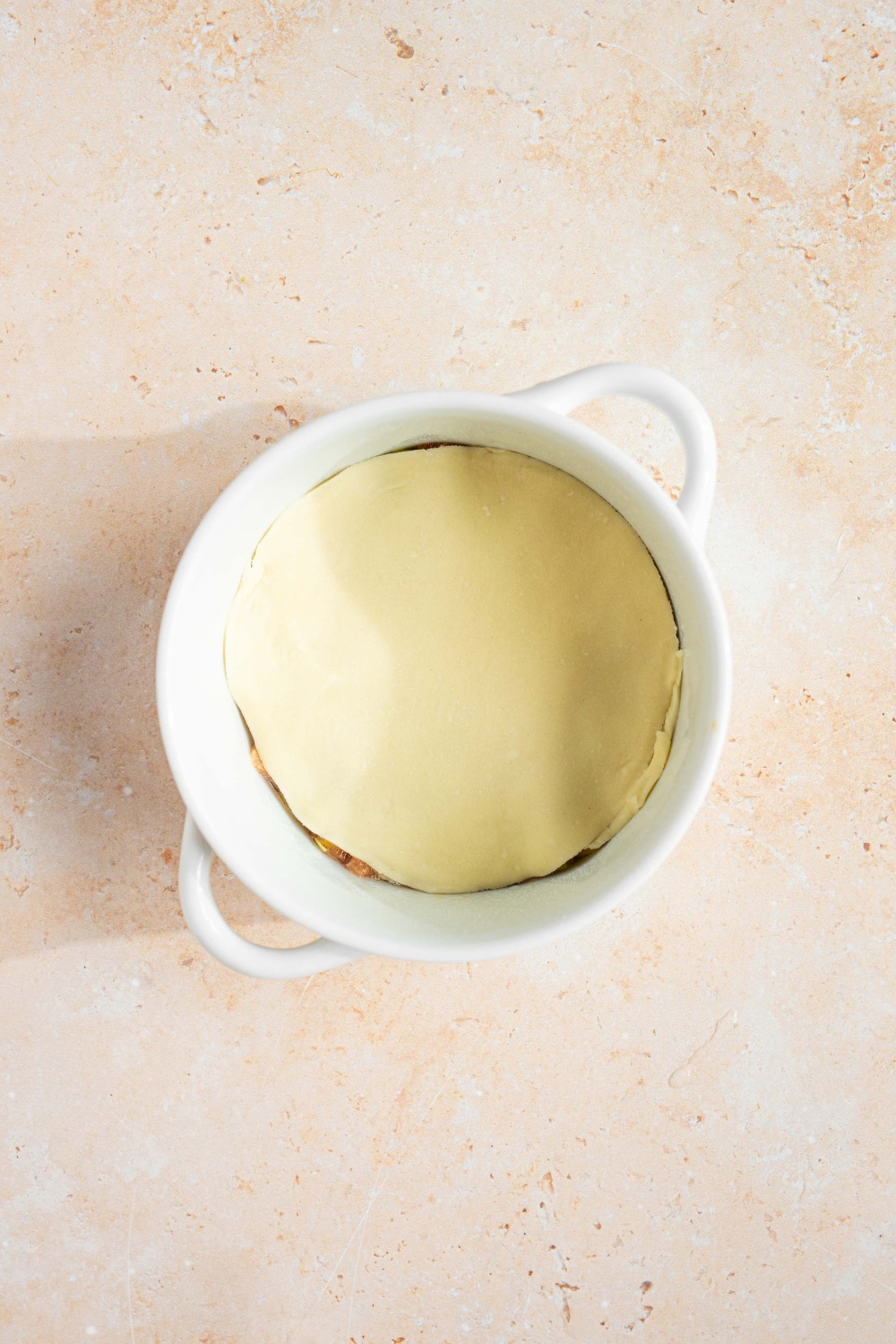 A ramekin with an uncooked dumpling lasagna layered with a pork mixture and wonton wrap. The ramekin is on a tan counter.