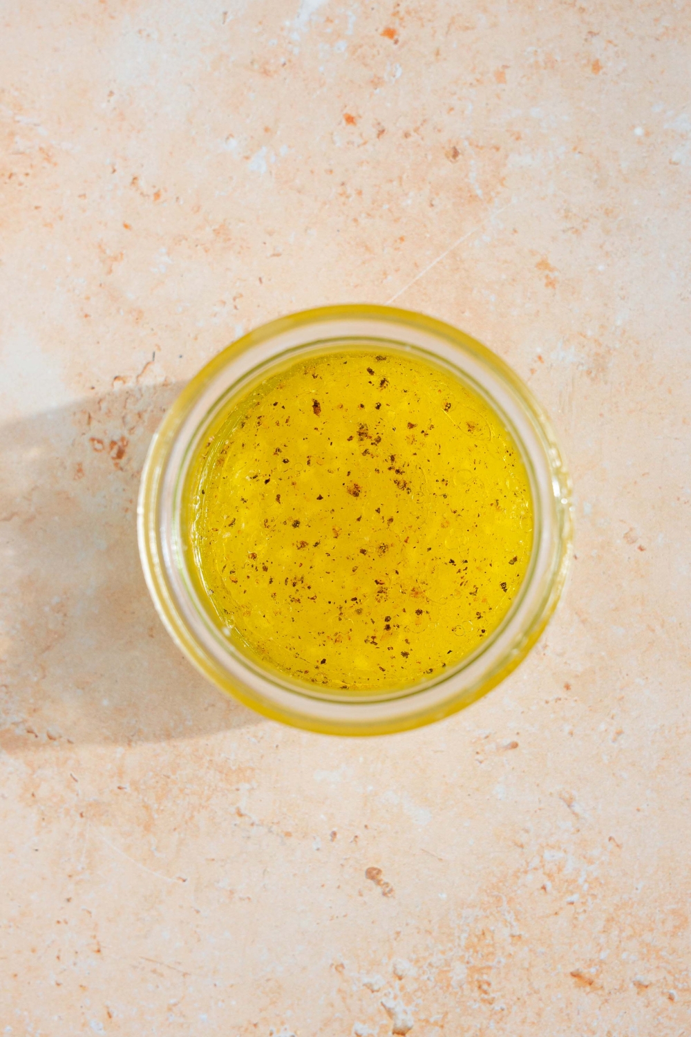 A glass jar with iceberg lettuce salad dressing made with lemon juice, oil, vinegar, garlic, salt, and pepper. The jar is on a tan counter.