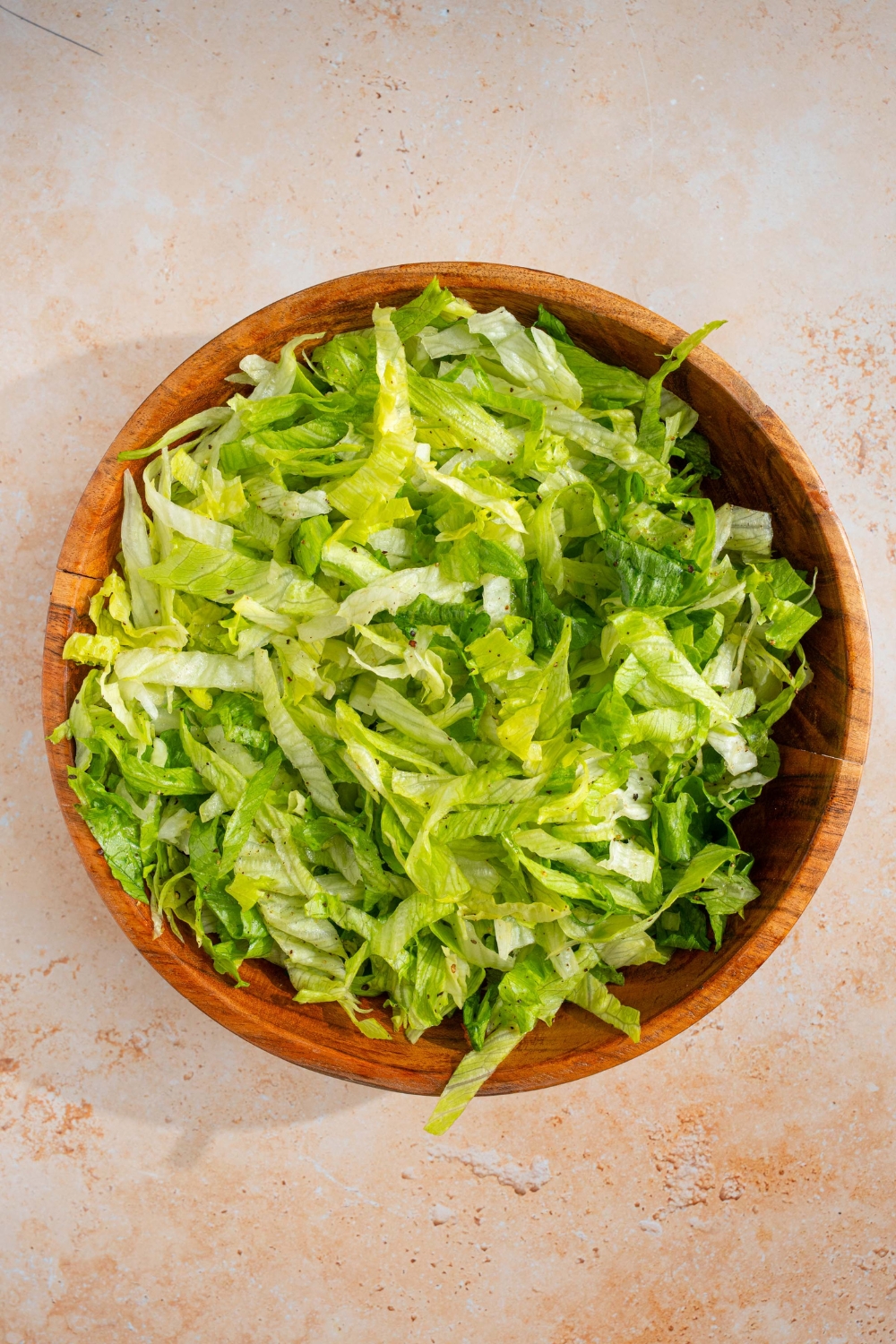 A wooden salad bowl with chopped iceberg lettuce. The bowl is on a tan counter.