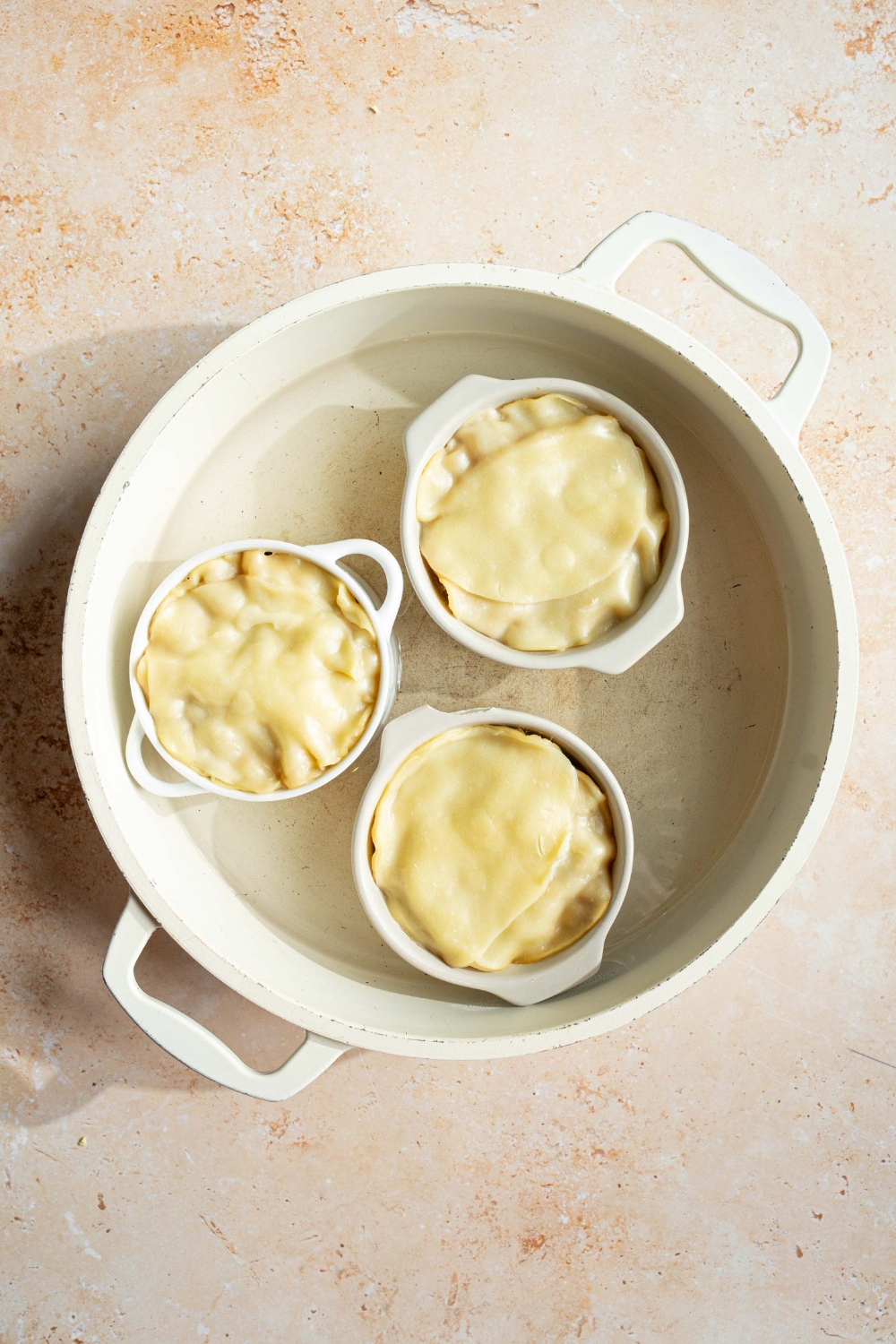 A large pot with water and three ramekins of steamed dumpling lasagnas. The pot is on a tan counter.