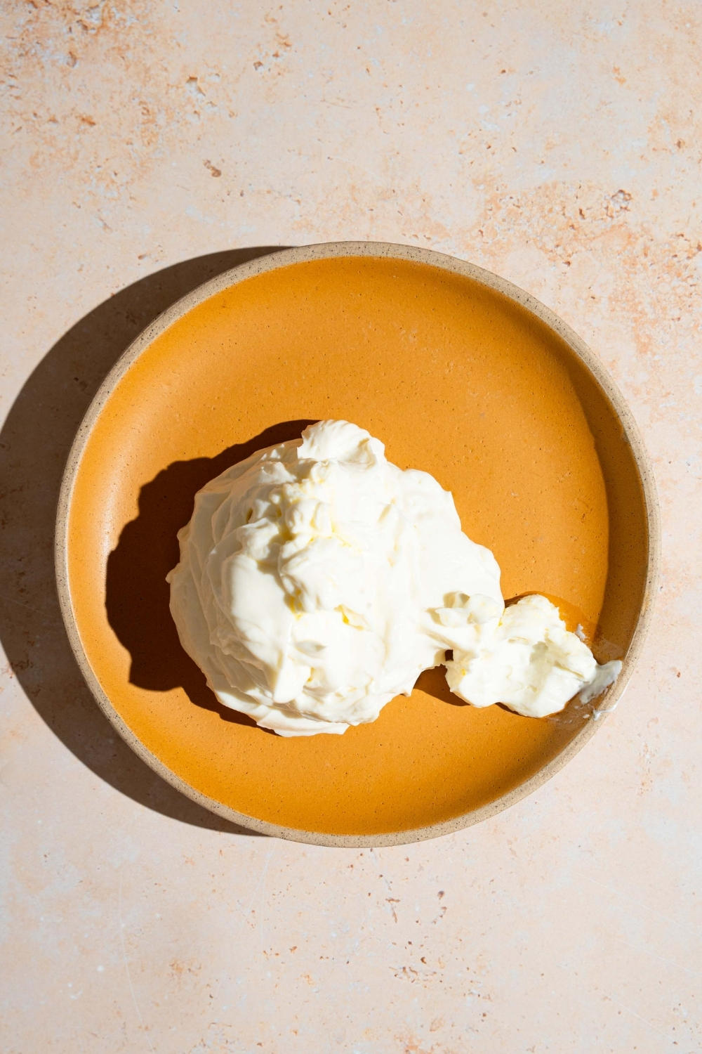 An orange plate with a pile of whipped ricotta dip. The plate is on a white counter.