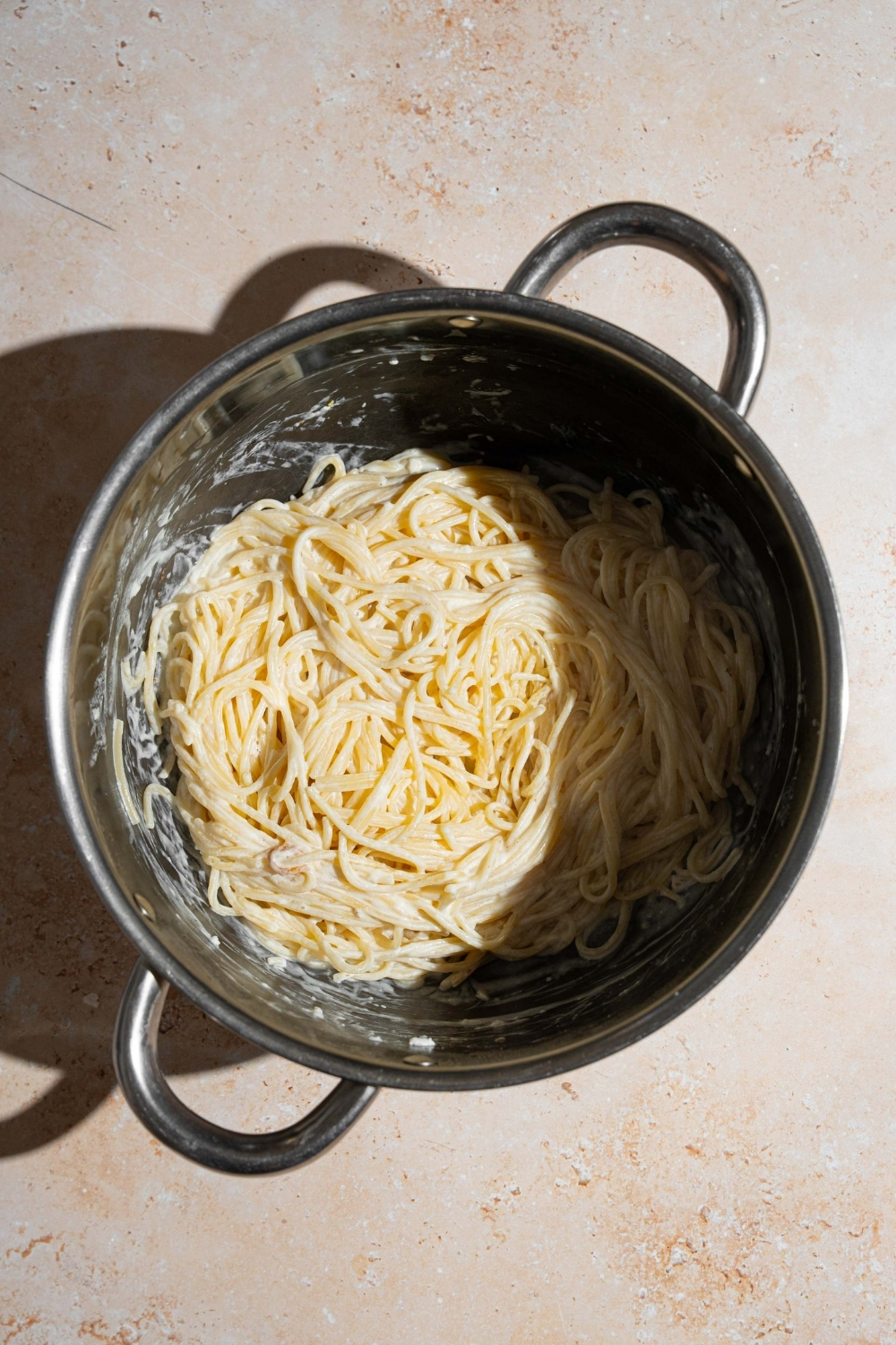 A stock pot with spaghetti tossed in Mexican white spaghetti sauce. The pot is on a tan counter.