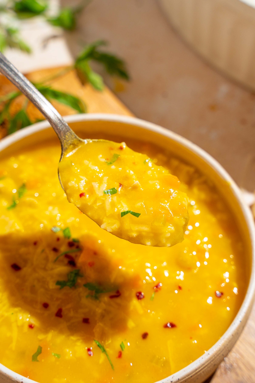 A white bowl of Italian penicillin soup garnished with fresh parsley and crushed red pepper. There is a spoon with a bite of soup. The bowl is on a wooden board on a tan counter.