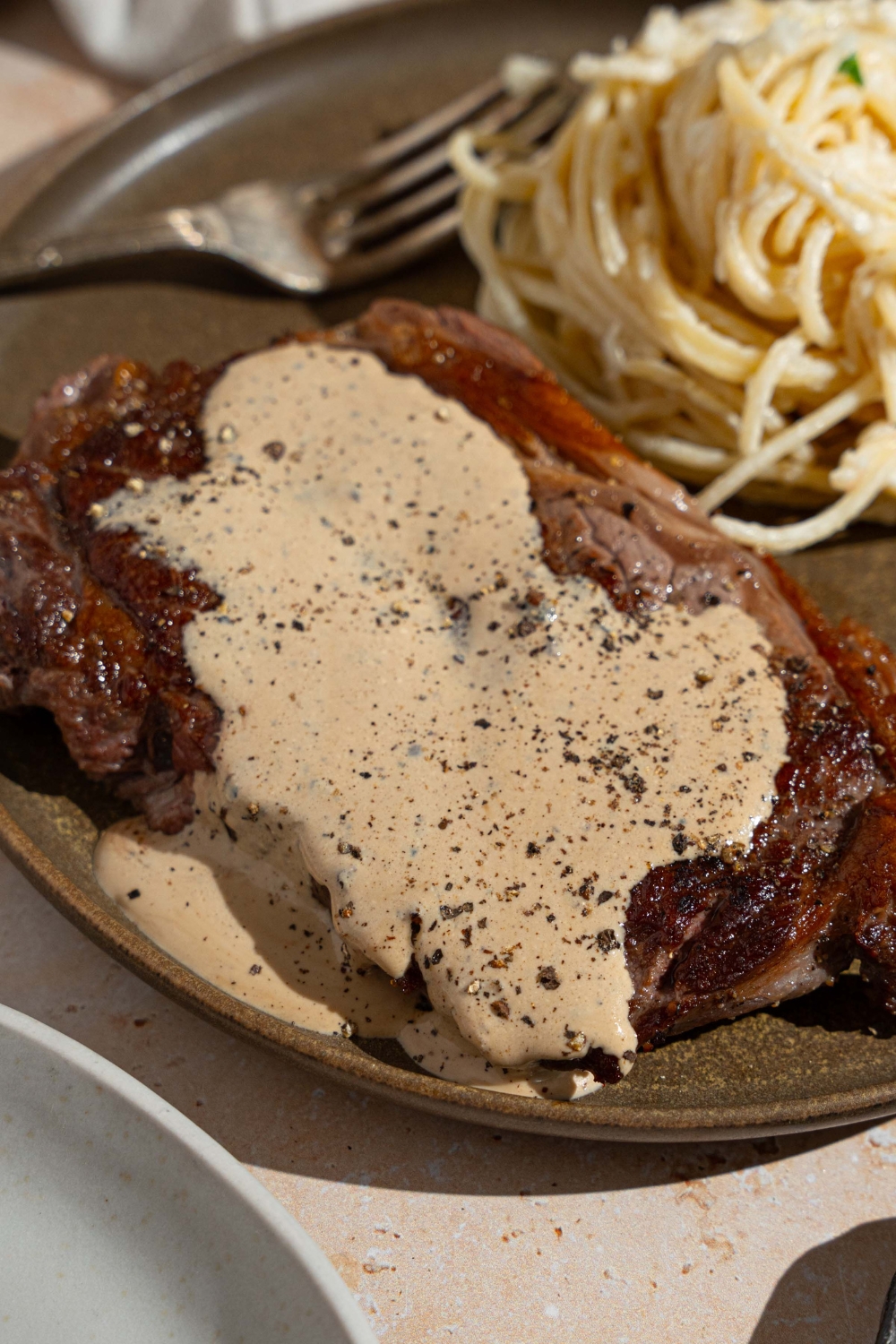 Peppercorn sauce served over steak. The steak is on a plate with a side of spaghetti. There is a fork on the plate.