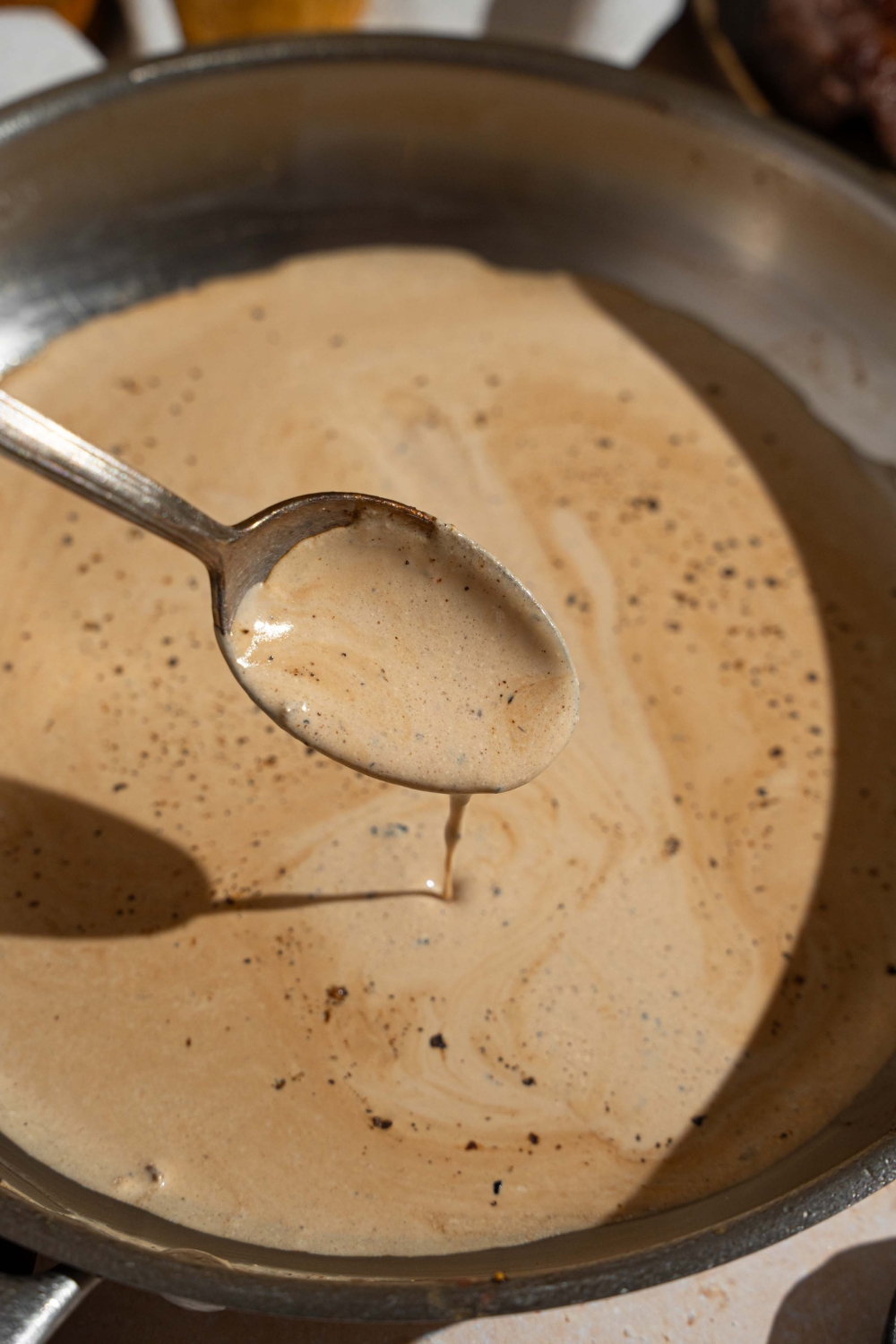 A skillet with peppercorn sauce. There is a spoon dipped in the sauce.