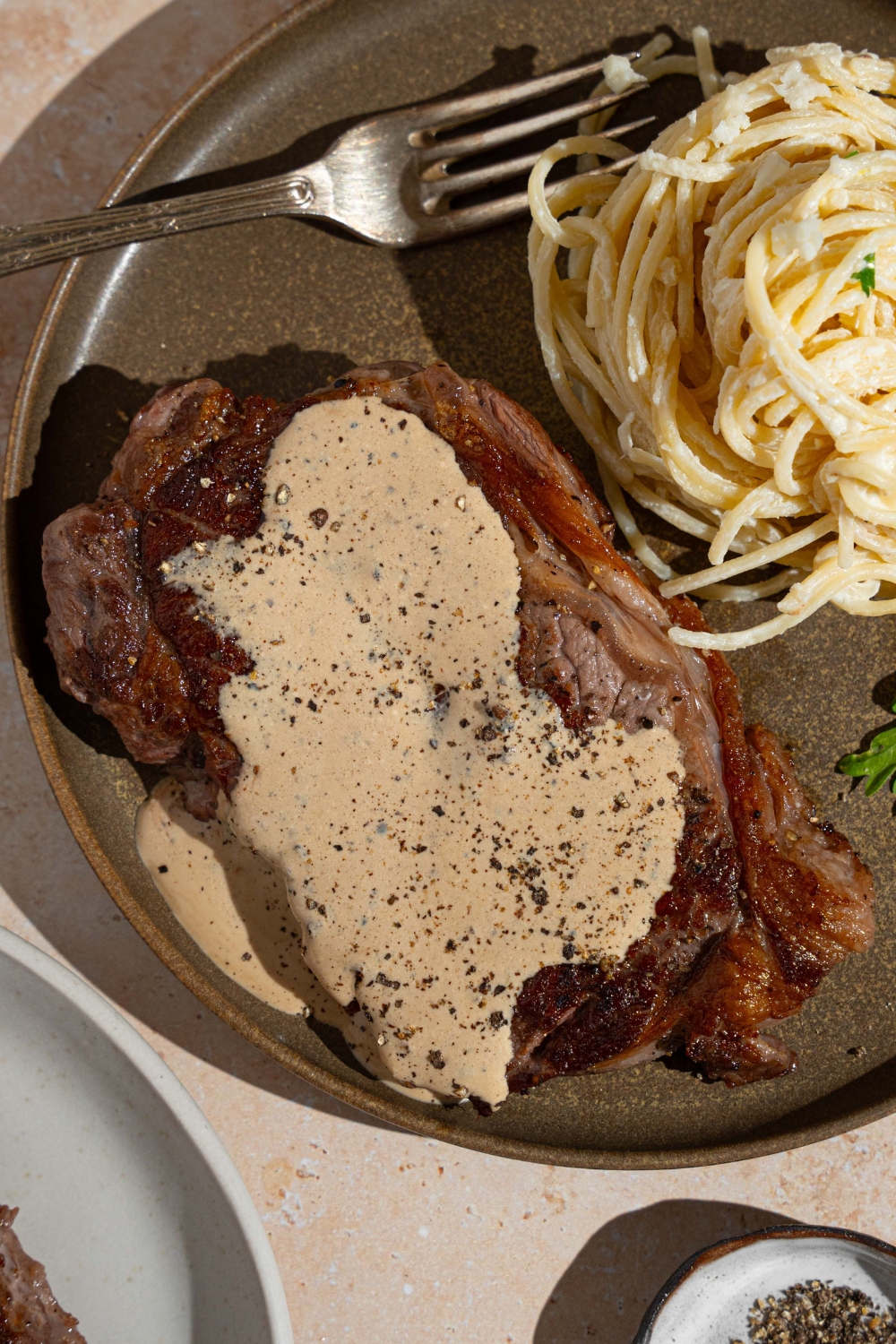Peppercorn sauce served over steak. The steak is on a plate with a side of spaghetti. There is a fork on the plate.