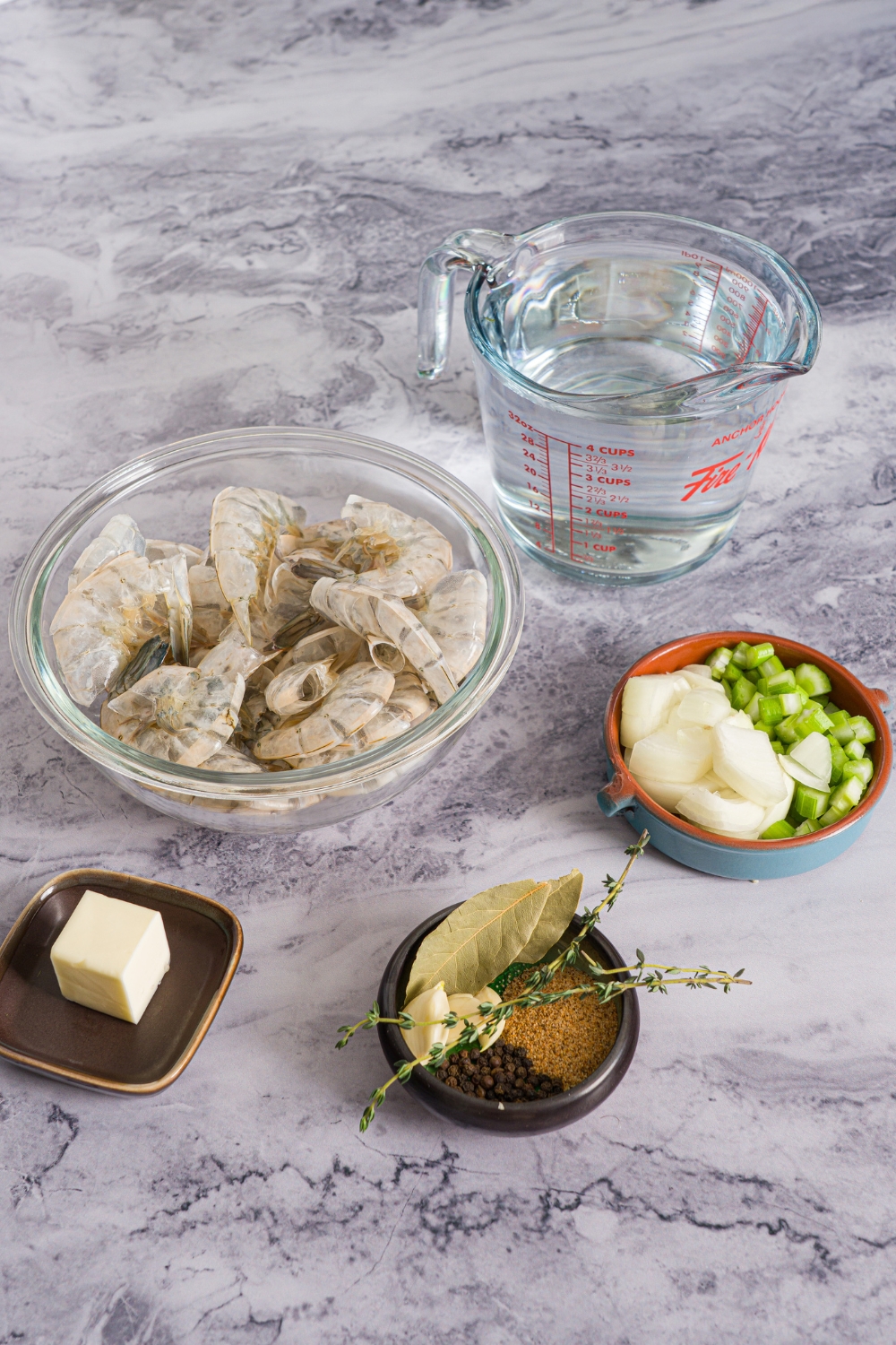 A marble counter with several ingredients to make shrimp stock including shrimp shells, water, diced onion and celery, butter, and seasonings.