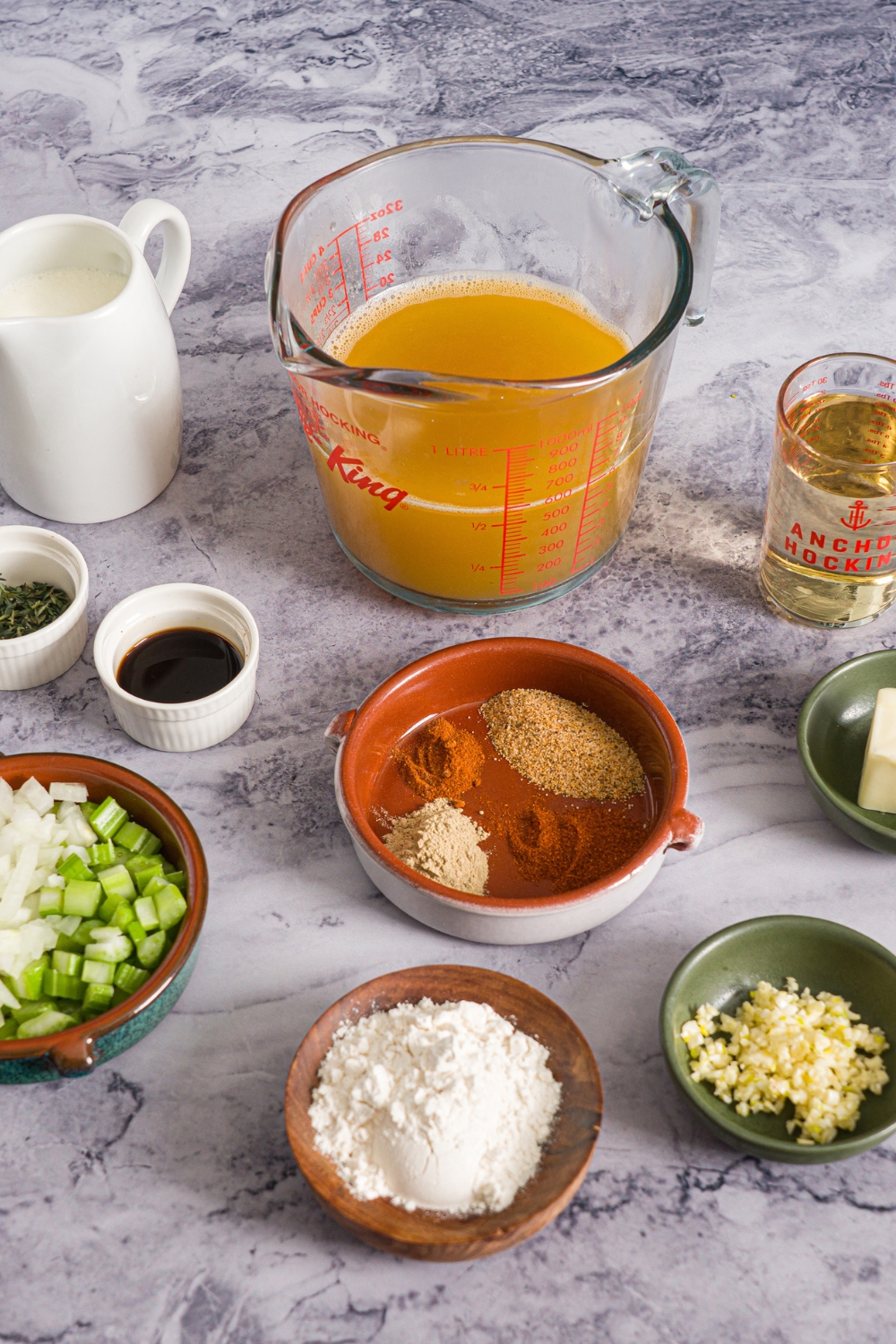 A marble counter with ingredients to make shrimp bisque including shrimp stock, flour, diced celery and onions, garlic, heavy cream, and seasonings.