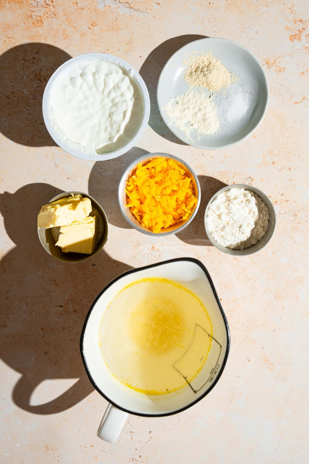 An overhead shot of several bowls in various sizes containing ingredients to make sour cream sauce including sour cream, shredded cheddar cheese, flour, chicken broth, butter, and seasonings.