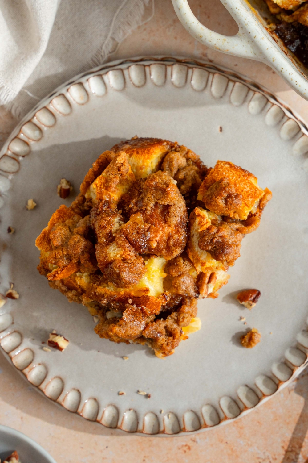 A white plate with a slice of sourdough french toast casserole. The plate is on a tan counter with a white cloth napkin.