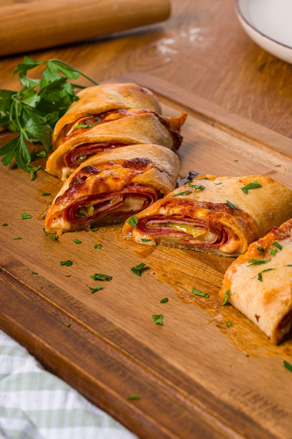 A wooden cutting board with sliced stromboli garnished with fresh parsley. The board is on a wood counter.