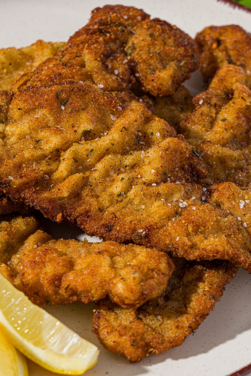 A white plate with breaded veal cutlets served with lemon wedges.