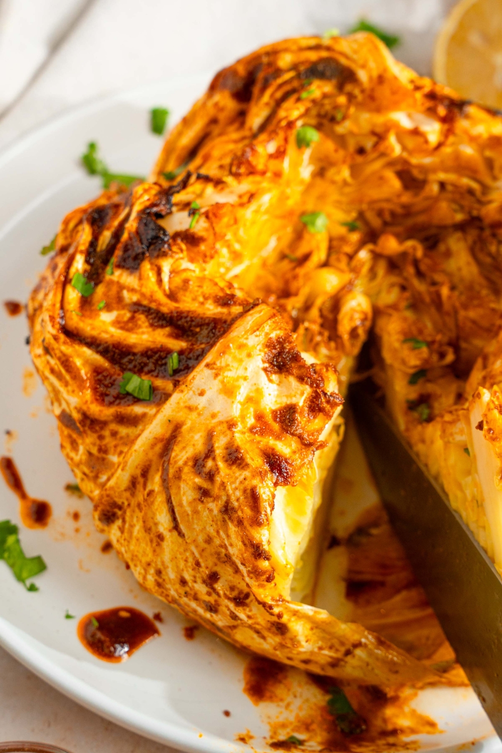 A white plate with a cabbage boil with seasoned with cajun spices and garnished with fresh parsley. A knife is slicing a bite of the cabbage.