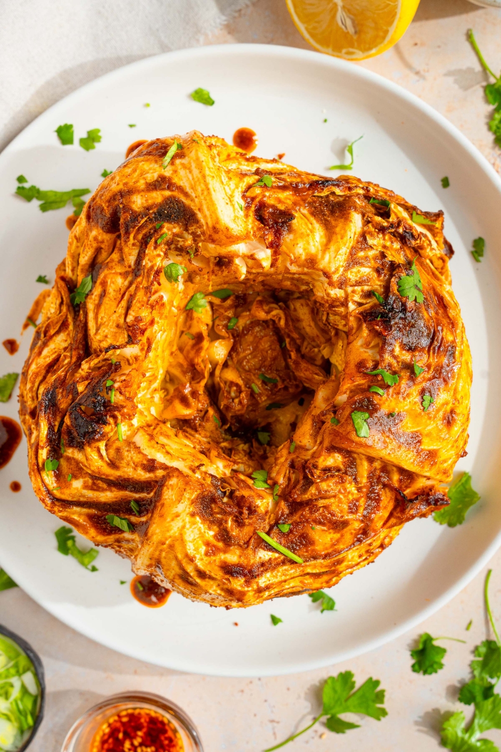 A white plate with a cabbage boil garnished with fresh parsley. The plate is on a tan counter with a small bowl of garnishes and lemon.