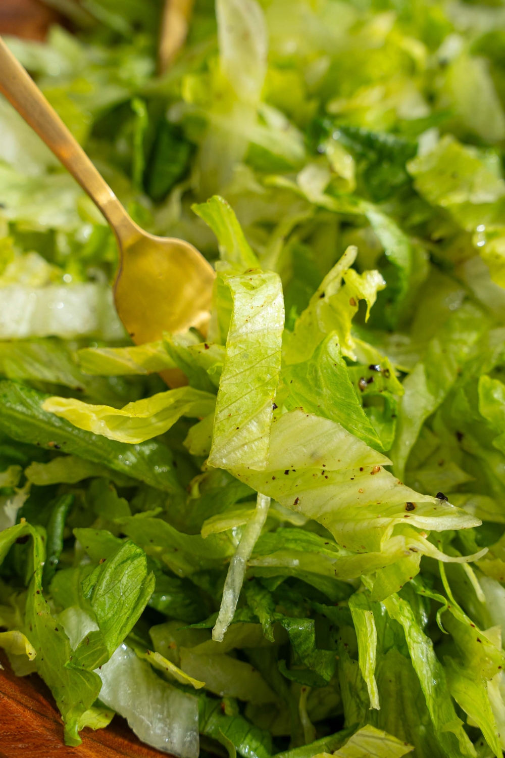 A wooden salad bowl with iceberg lettuce salad tossed in lemon dressing. There is a fork in the bowl.