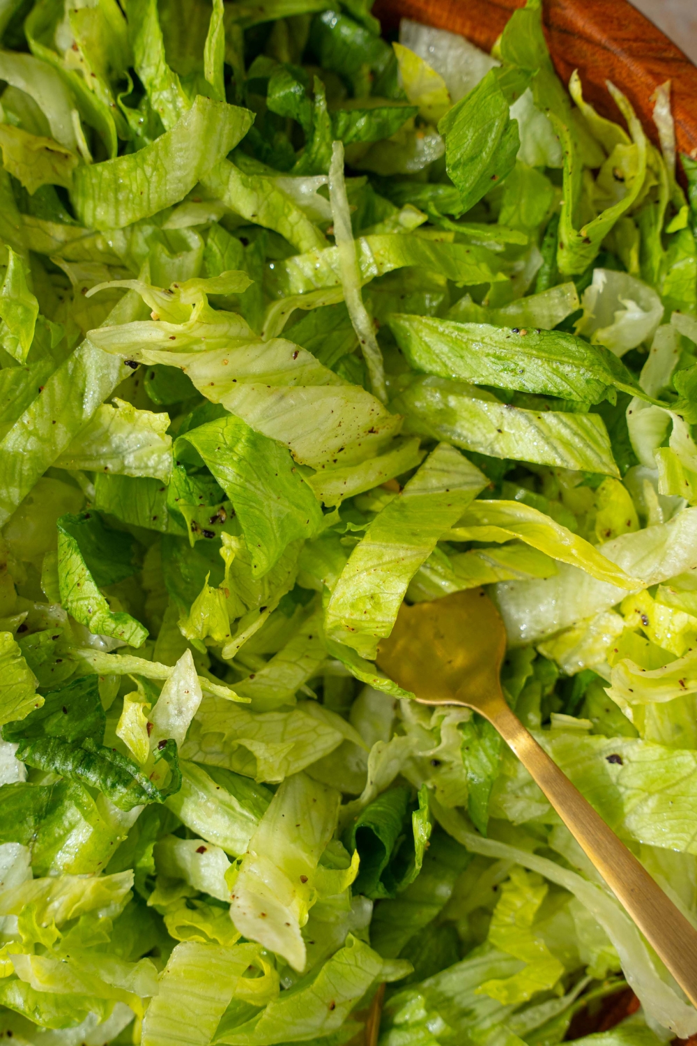 A wooden salad bowl with iceberg lettuce salad tossed in lemon dressing. There is a fork in the salad.