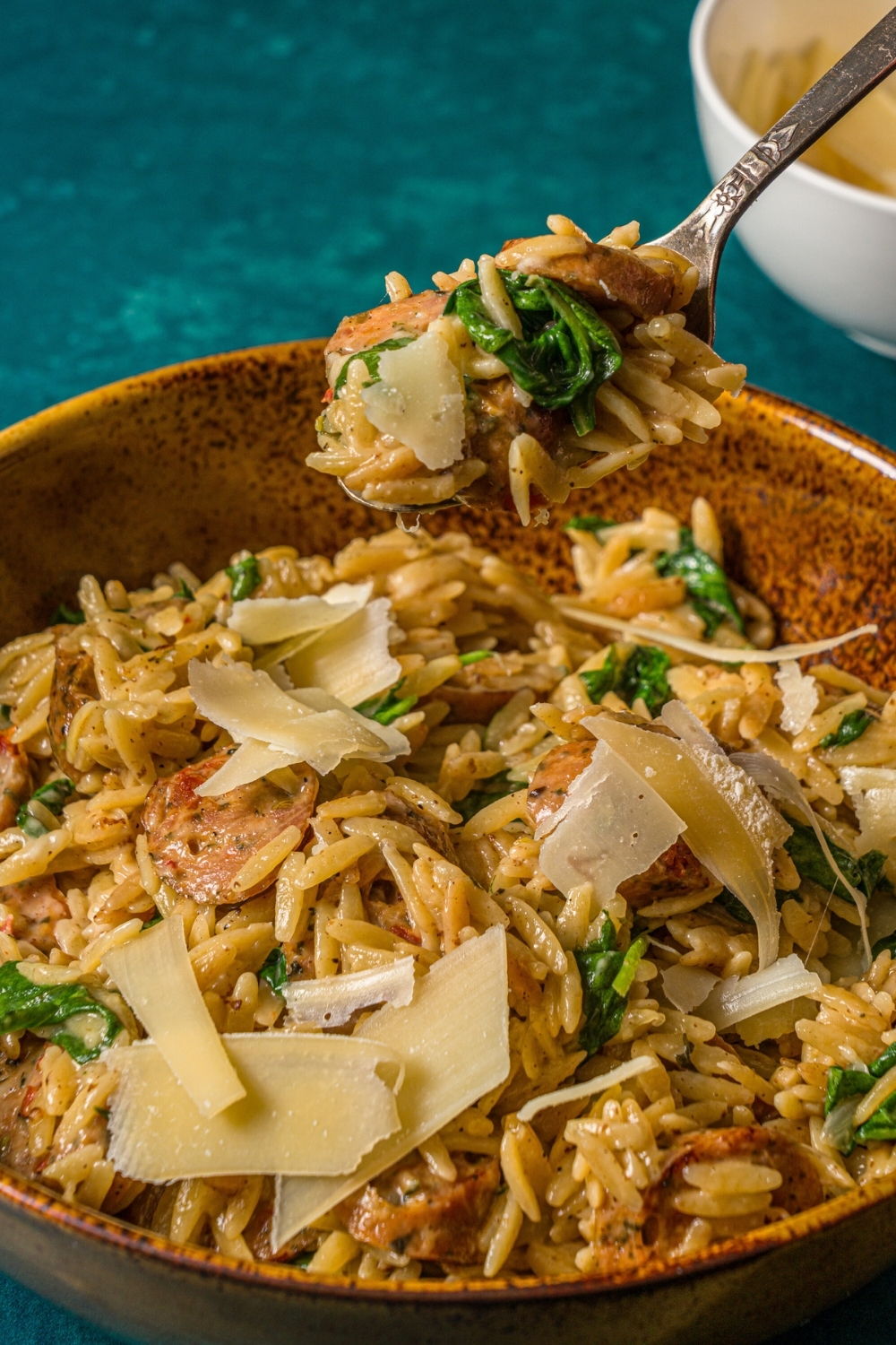 A spoon with some chicken sausage orzo on it above a bowl filled with the orzo.
