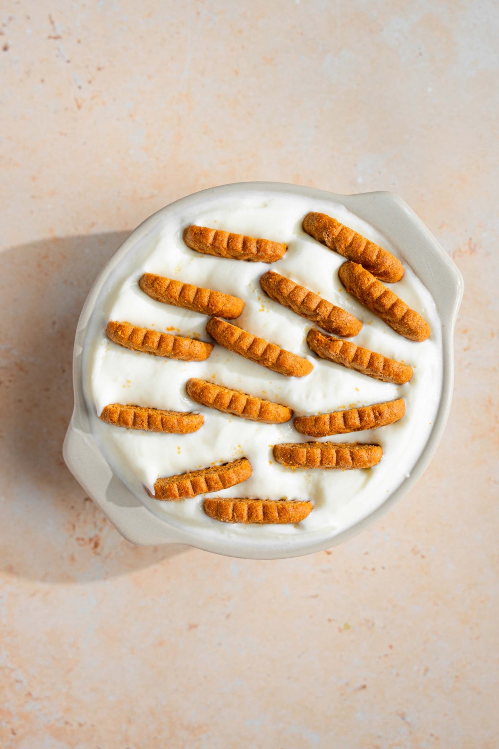 Biscoff cookies in a tub of yogurt on a white counter.