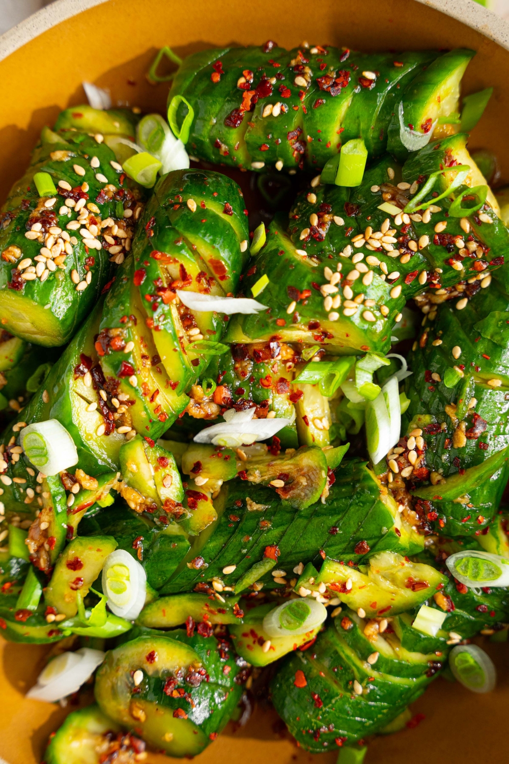 A bowl of spicy Asian cucumber salad tossed in dressing and garnished with slice green onions, crushed red pepper, and sesame seeds.