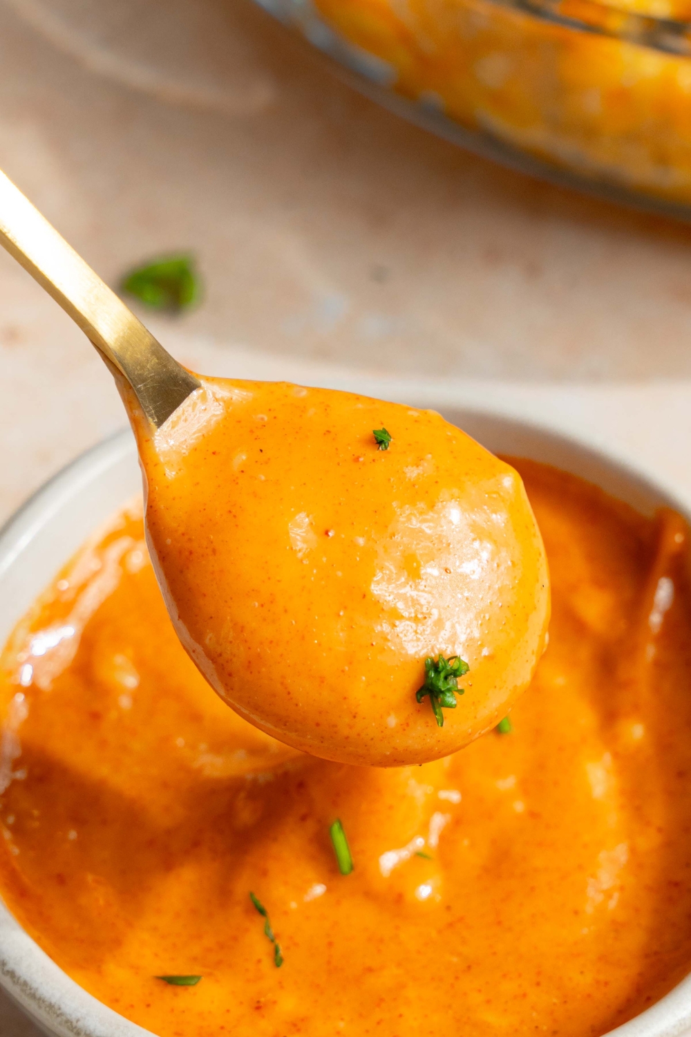 A spoon dipped into a white bowl with campfire sauce garnished with fresh parsley. The bowl is on a tan counter.
