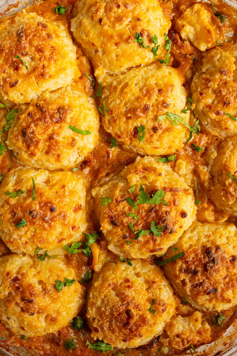 A round baking dish with baked cheddar bay biscuit chicken pot pie garnished with fresh parsley.