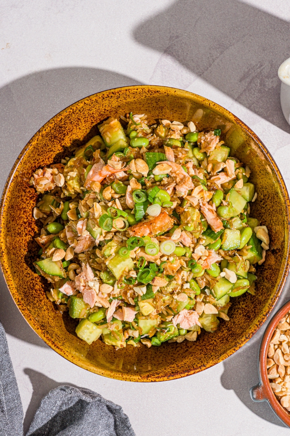 A bowl of crispy rice salmon salad with honey ginger dressing garnished with sliced green onion. The bowl is on a marble counter with a gray cloth napkin.