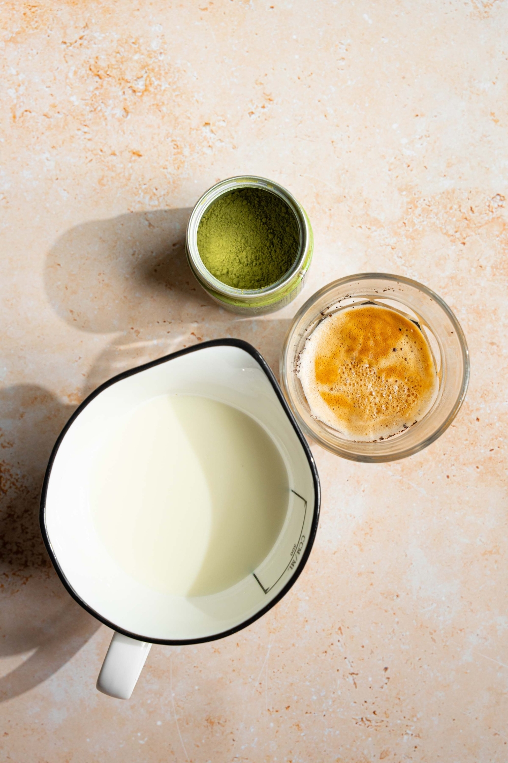 An overhead shot of ingredients to make a dirty matcha latte including matcha powder, espresso, and milk.