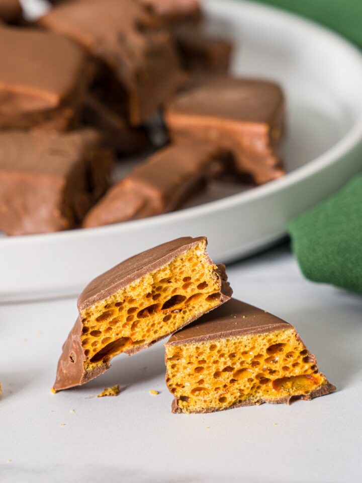 A sliced piece of sponge candy on a marble counter with a white plate of sponge candy and green cloth napkin.