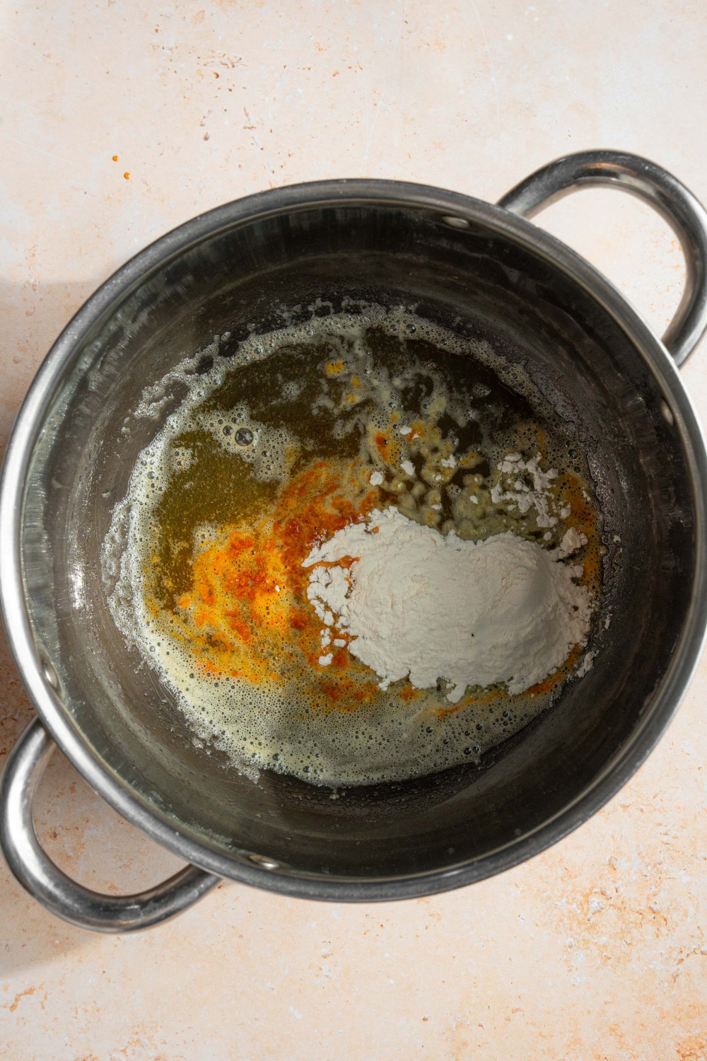 A pot with melted butter, flour, and seasonings. The pot is on a tan counter.