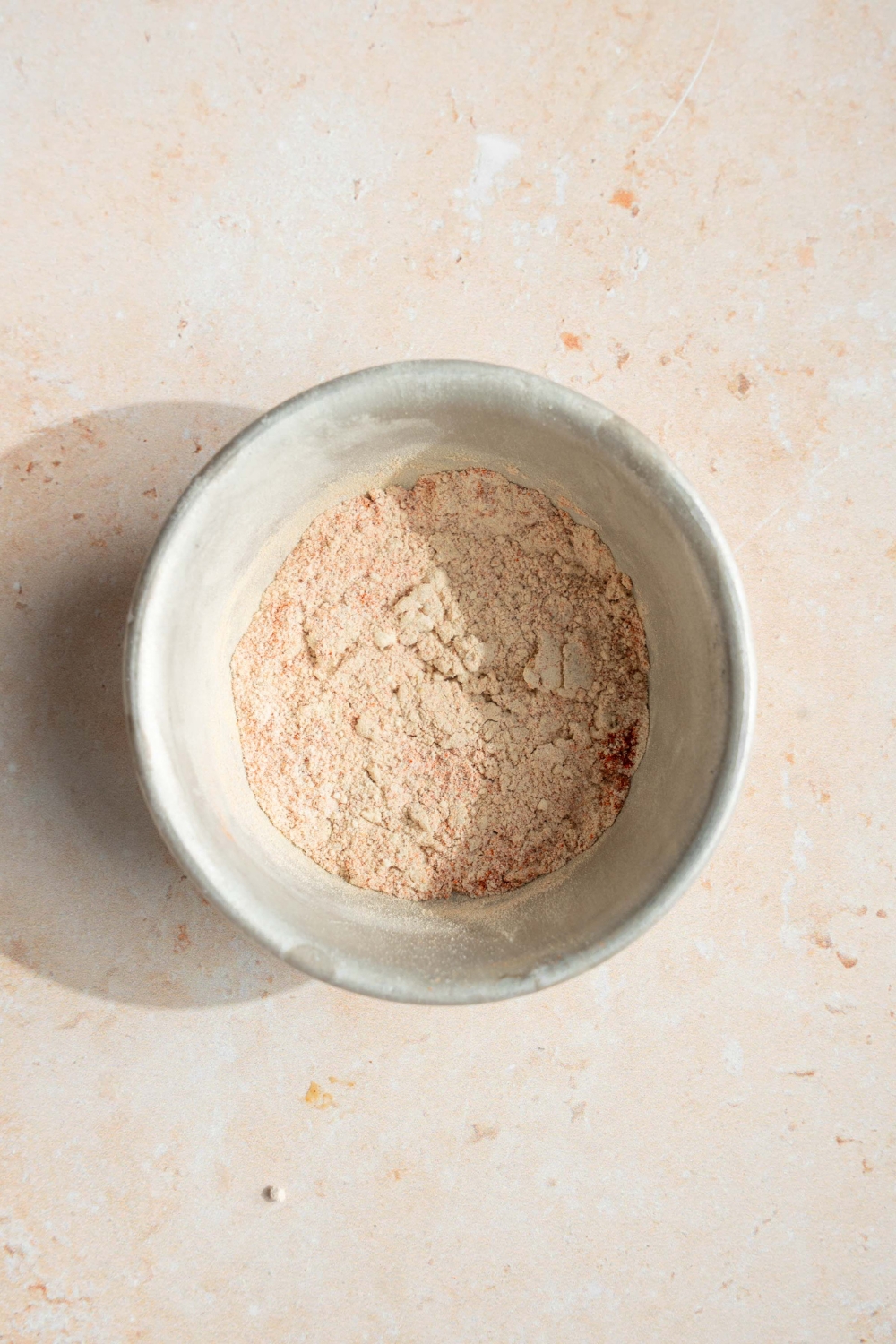 A small bowl with a blend of seasonings including garlic powder, onion powder, and paprika. The bowl si on a tan counter.
