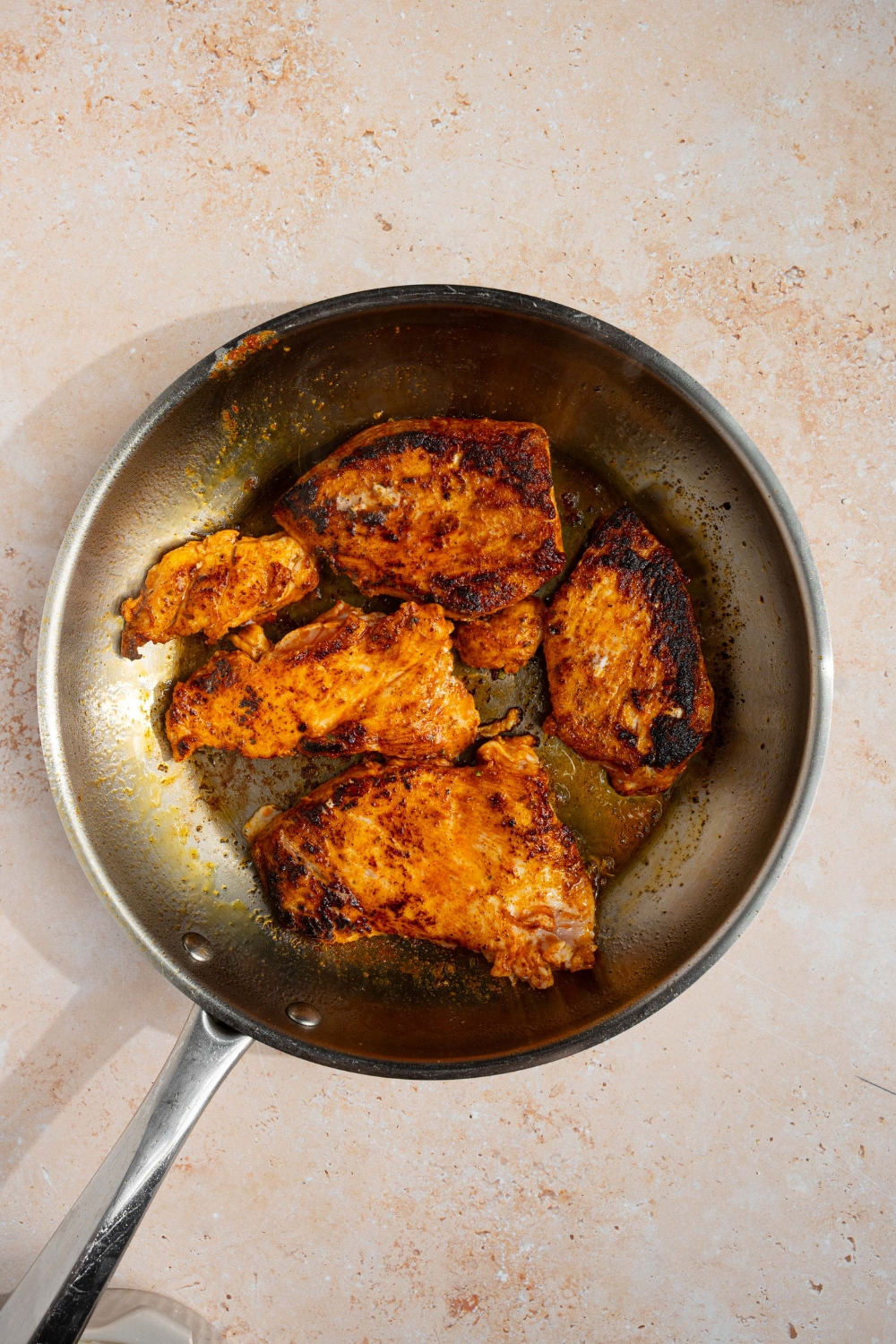 A skillet with seasoned chicken cooking in oil. The skillet is on a tan counter.