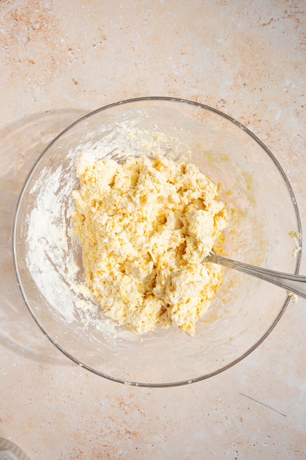 A large white bowl with a spoon mixing cheddar bay biscuit dough. The bowl is on a tan counter.