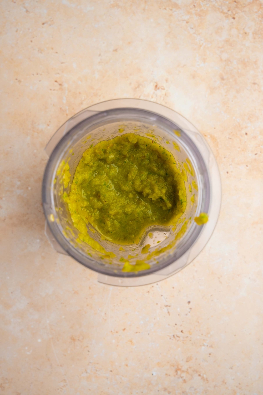A blender jar with blended jalapenos and green chiles. The jar is on a tan counter.