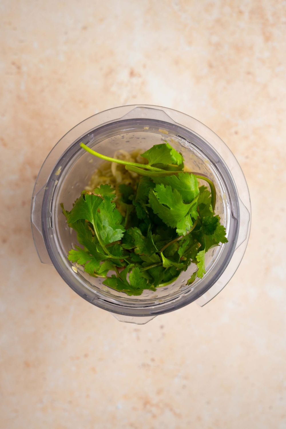 A blender jar with green chiles, jalapenos, and cilantro. The jar is on a tan counter.