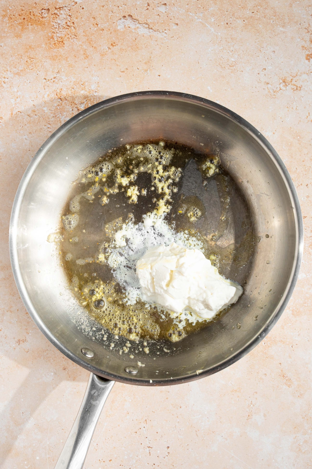 A skillet with sautéed garlic, butter, and cream cheese. The skillet is on a tan counter.