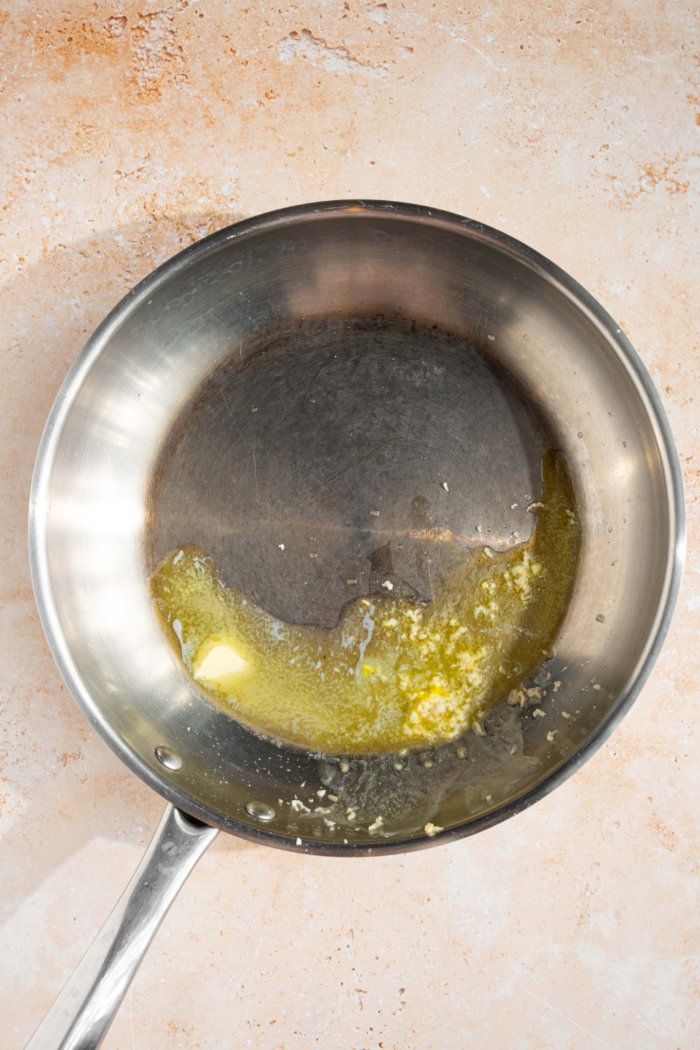 A skillet with melted butter and garlic. The skillet is on a tan counter.