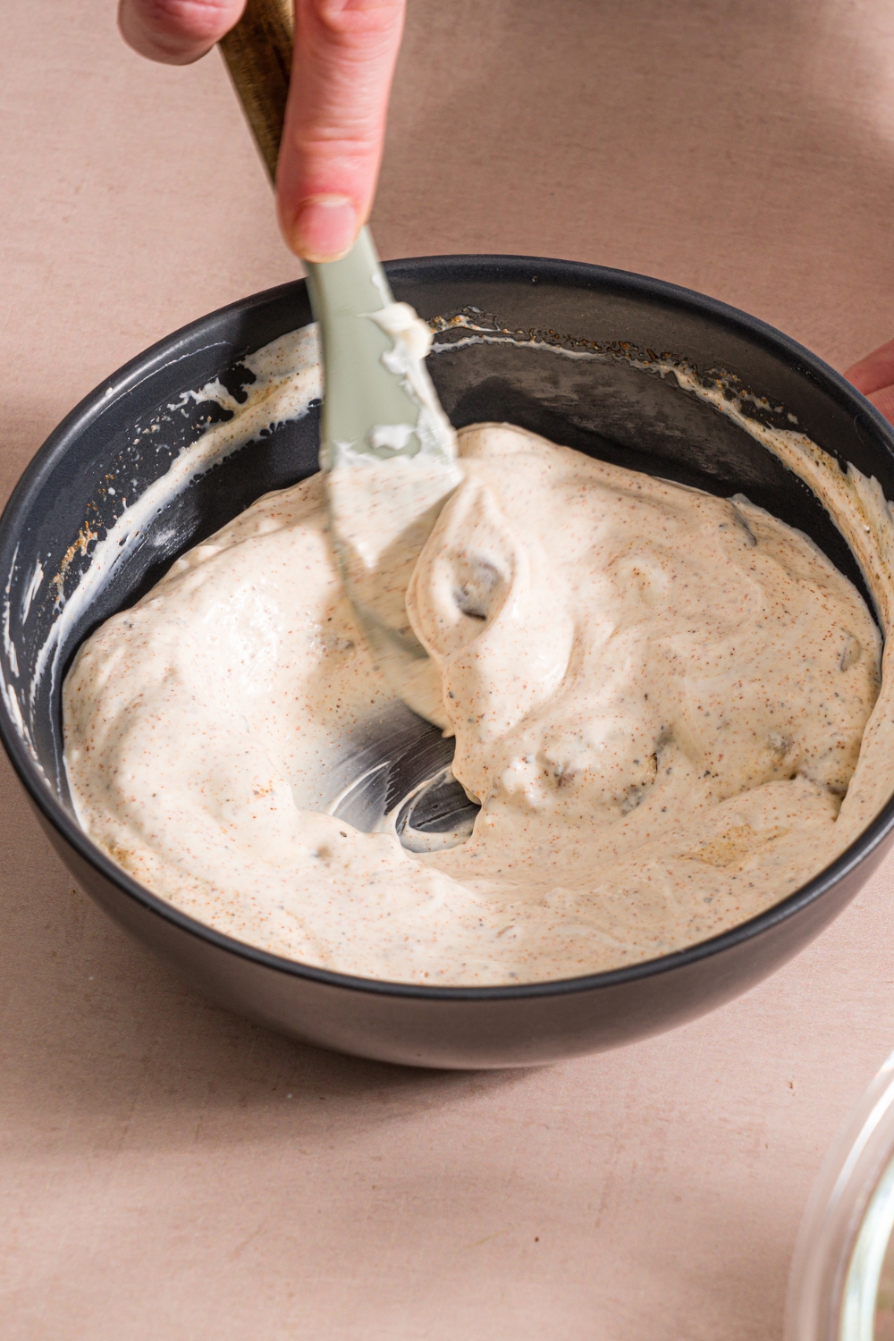 A black bowl with a spatula mixing ingredients to make garlic paprika dressing. The bowl is on a tan counter.