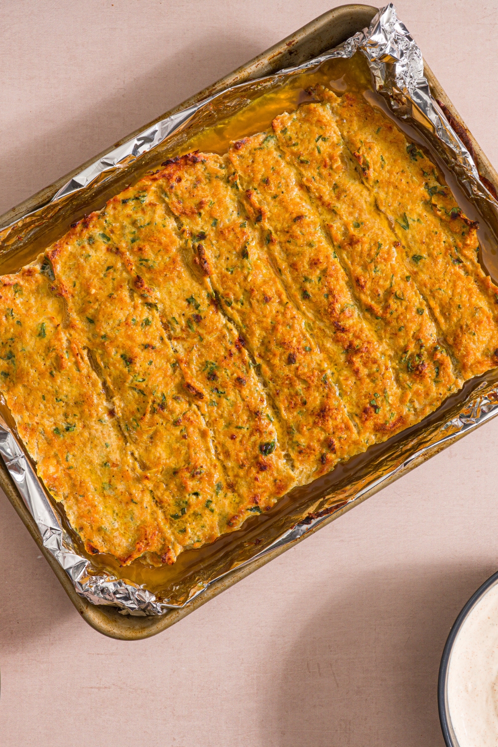 A baking sheet lined with foil with baked chicken kefta. The sheet is on a tan counter.