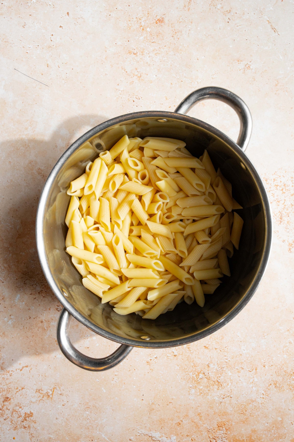 A pot with cooked penne pasta. The pot is on a tan counter.