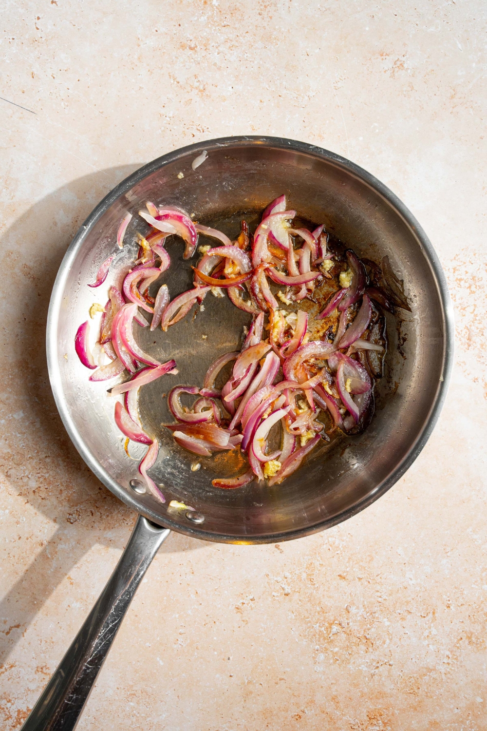 A skillet with sliced onion and garlic sautéing in butter. The skillet is on a tan counter.