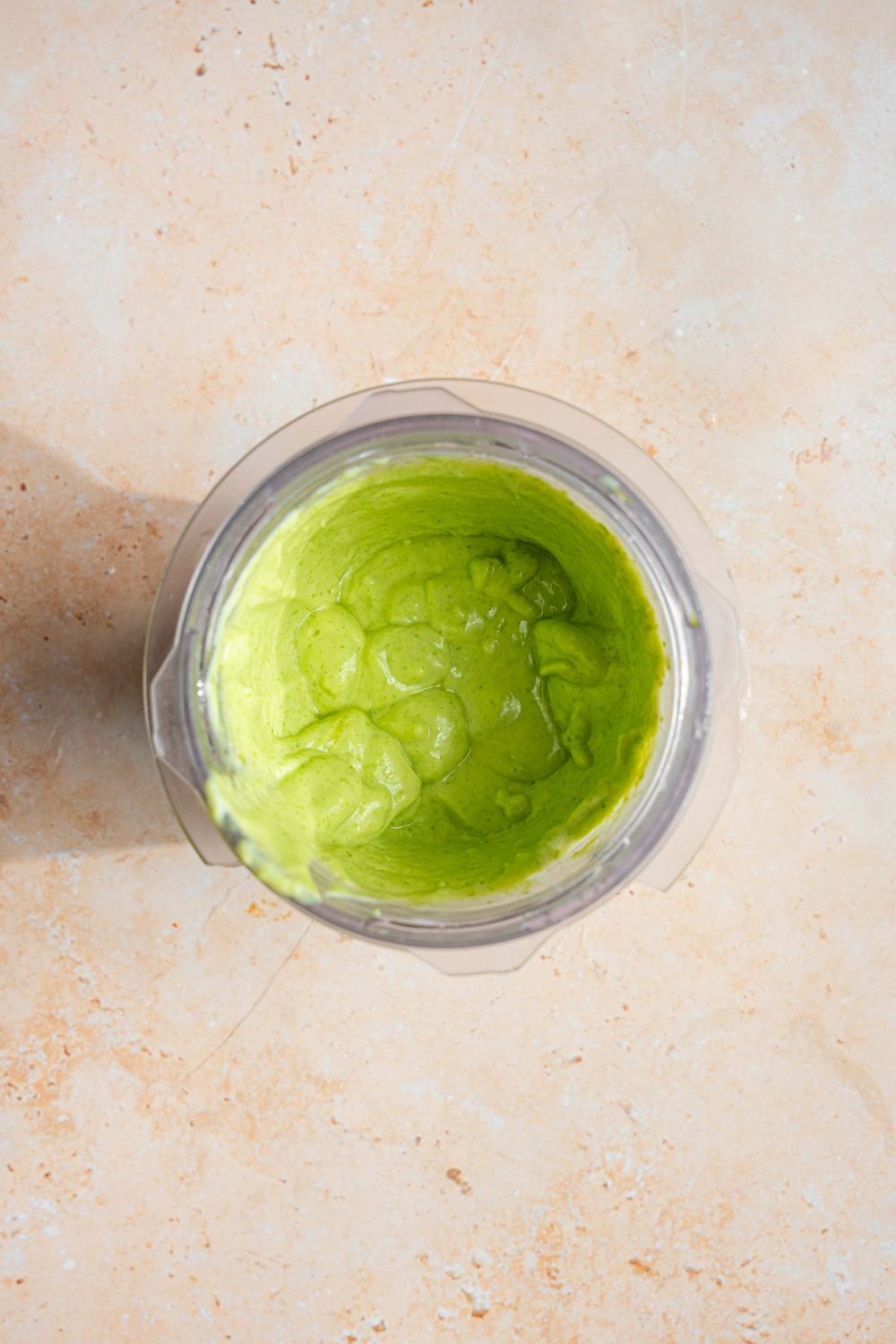 A blender jar with blended cilantro lime crema on a tan counter.