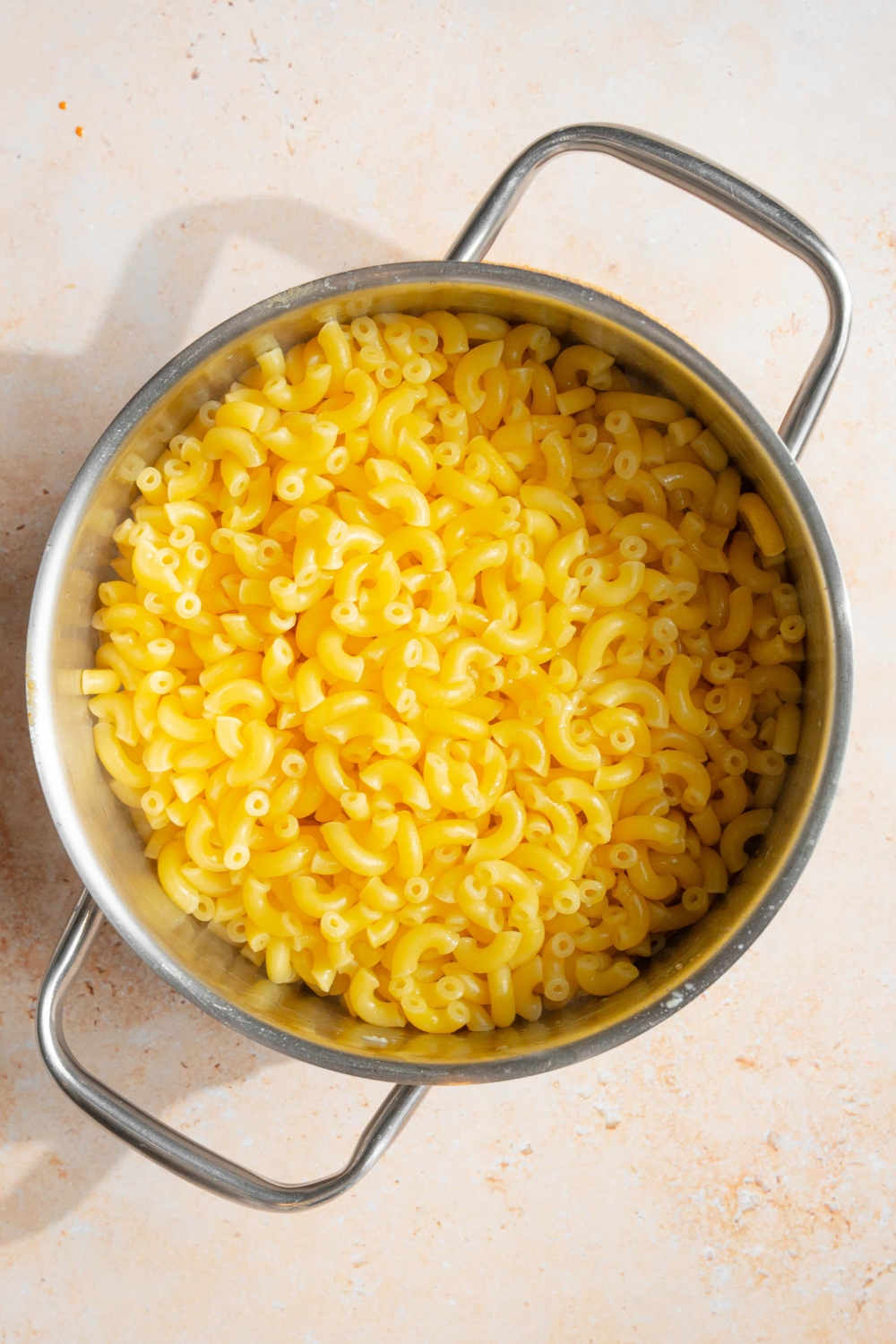 A pot with three cheese sauce topped with elbow pasta. The pot is on a tan counter.