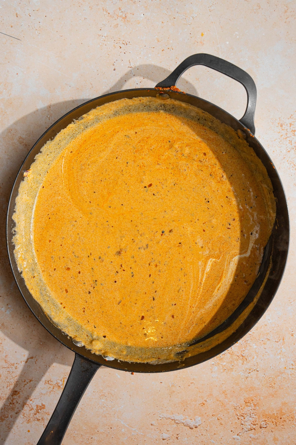A skillet with garlic parmesan sauce. The skillet is on a tan counter.