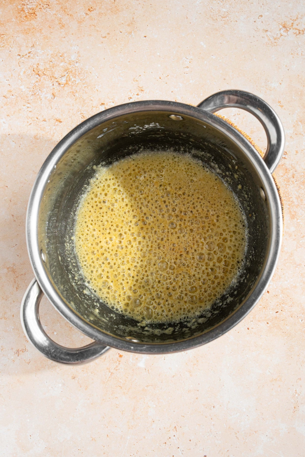 A pot with bubbling butter. The pot is on a tan counter.