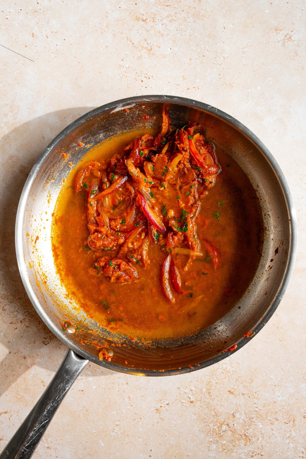 A skillet with blush sauce base including sautéed onions, garlic, tomato paste, and white wine. The skillet is on a tan counter.