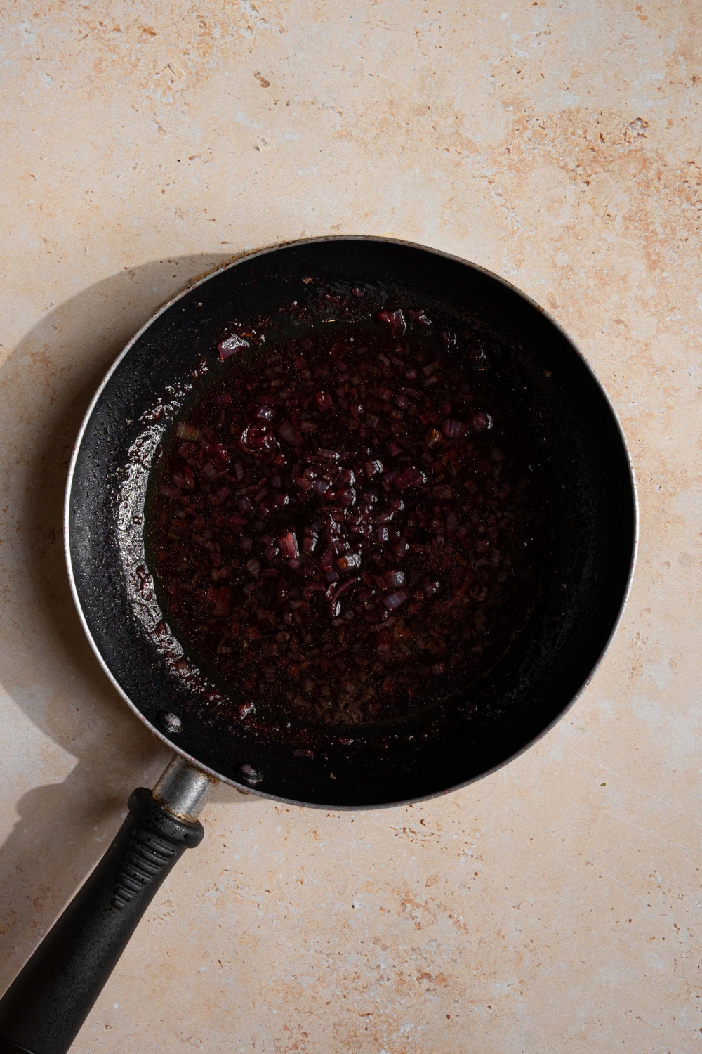 A skillet with a reduced sherry sauce mixture. The skillet is on a tan counter.