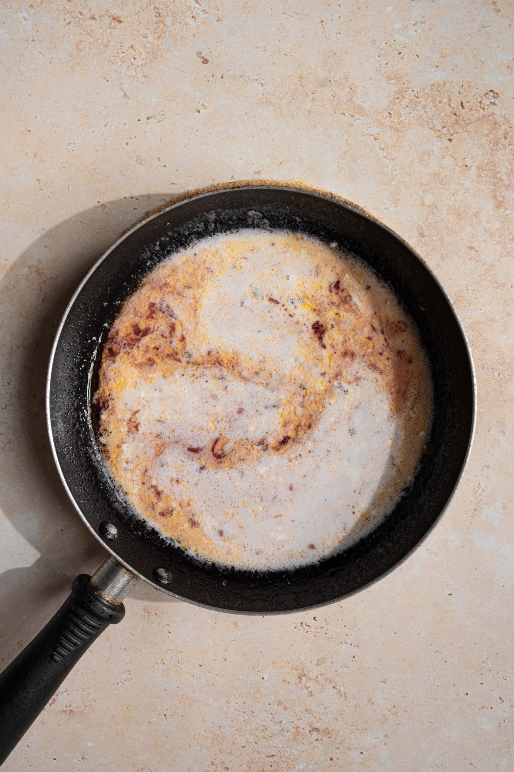 A skillet with cream added to a sherry sauce base. The skillet is on a tan counter.